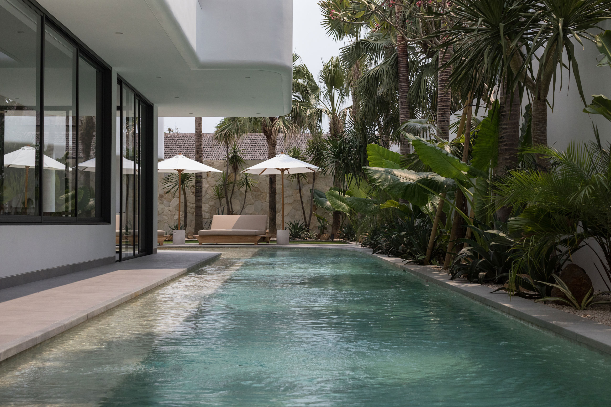 Poolside sun loungers and umbrellas surrounded by tropical garden at Jipsi Villas Bali
