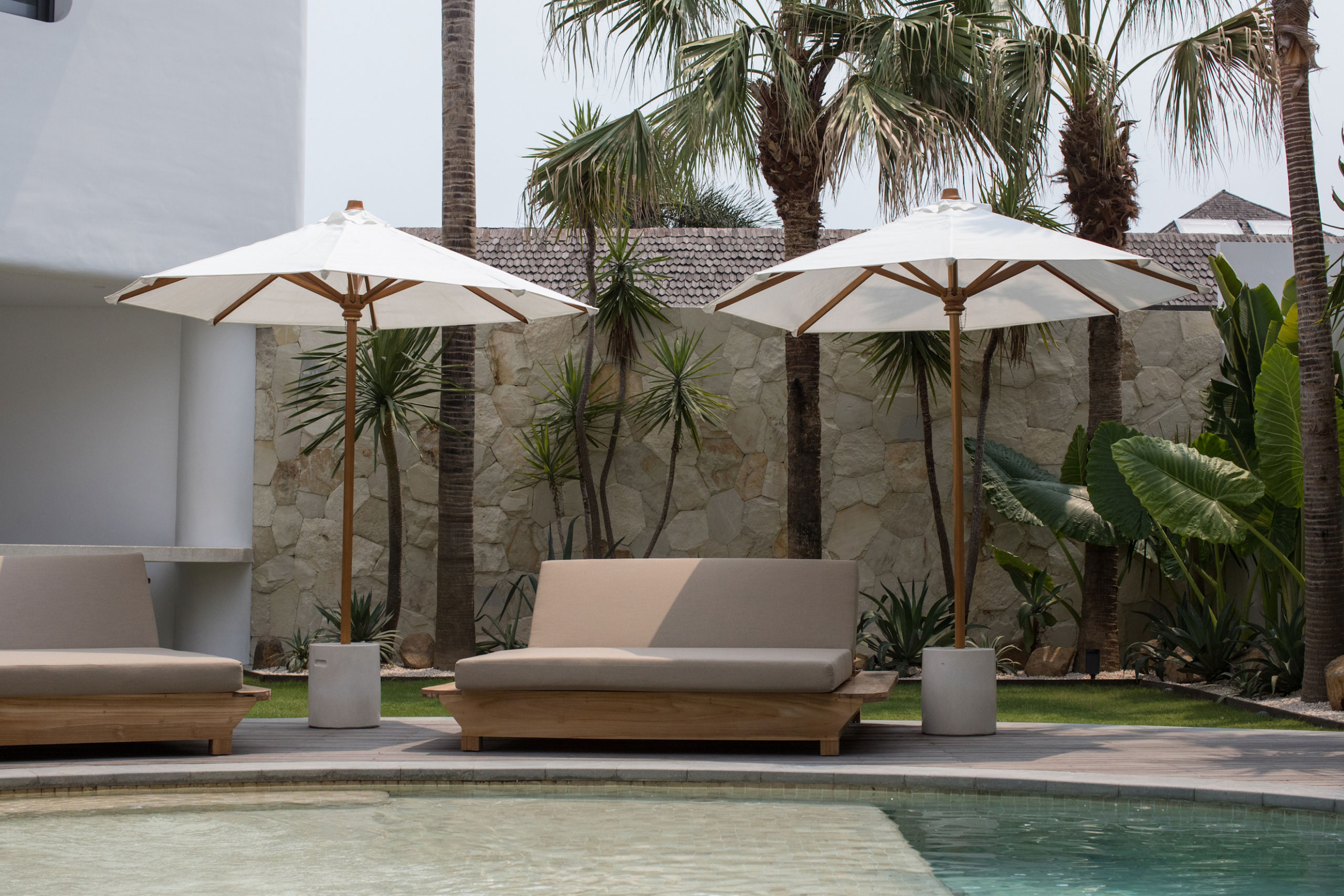 Poolside sun loungers and umbrellas surrounded by tropical garden at Jipsi Villas Bali
