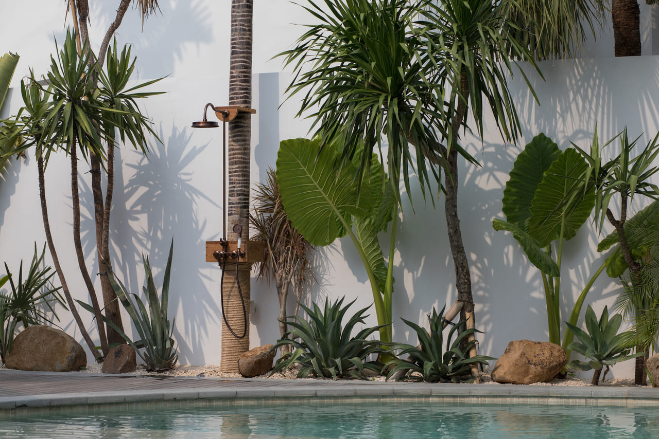Outdoor tropical shower by the pool surrounded by palm trees and lush greenery at Jipsi Villas Bali.